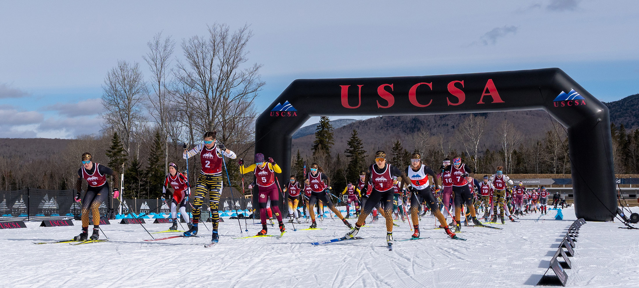 Women’s 15 km freestyle mass start begins under the USCSA arch at Mt. Van Hoevenberg, with a packed field of collegiate skiers launching into the race in Lake Placid.